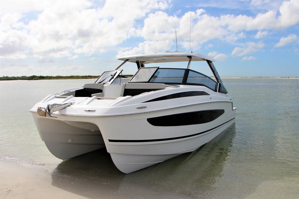A modern white boat with black accents anchored in shallow water, surrounded by a sandy shoreline and blue skies.